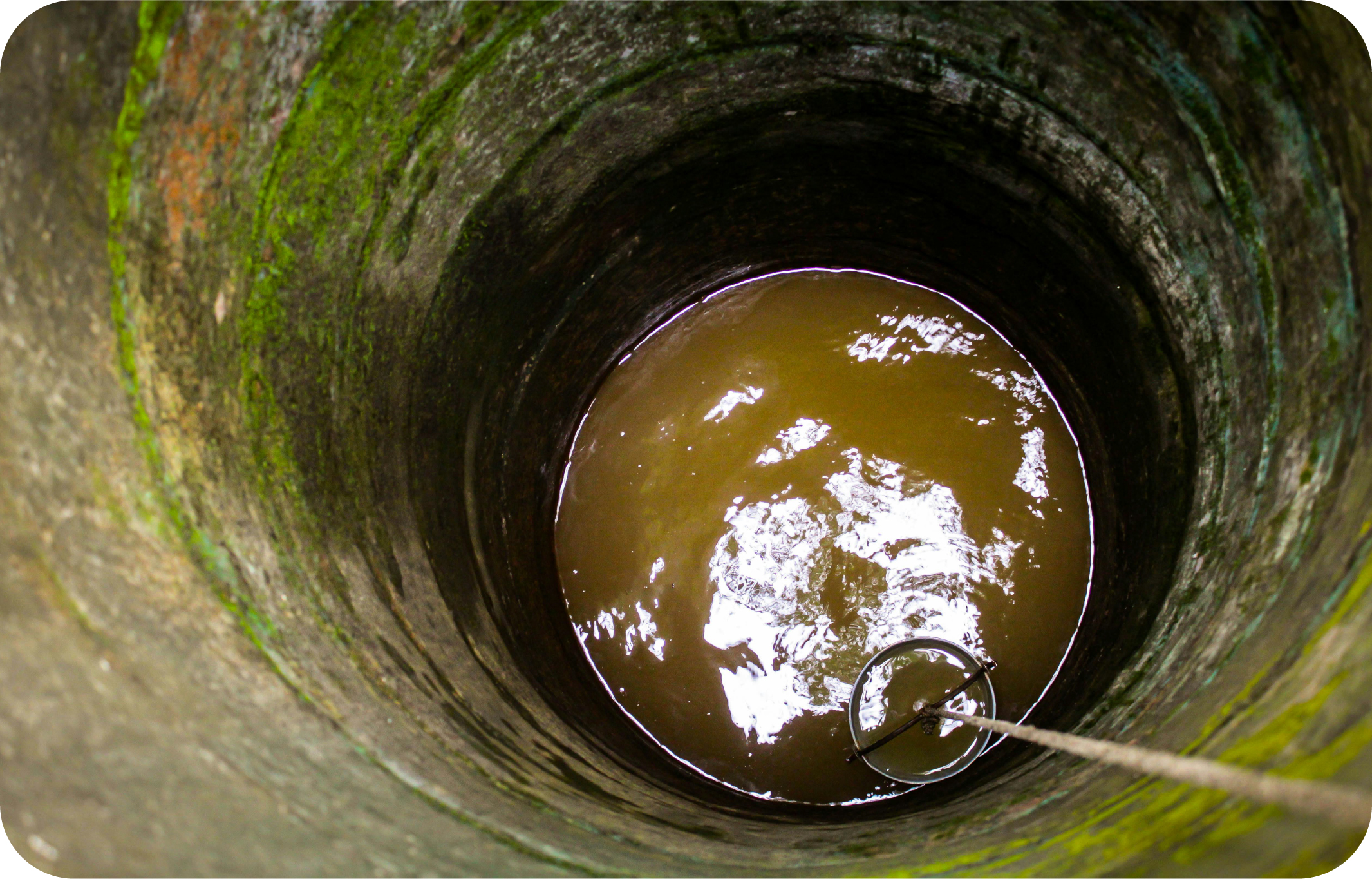 An image of the inside of an old water well with a bucket dipping into murky brown well water.